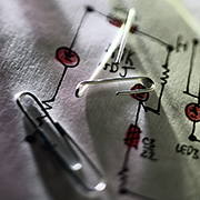 Photograph of paper clips on top of a hand-drawn electrical diagram.